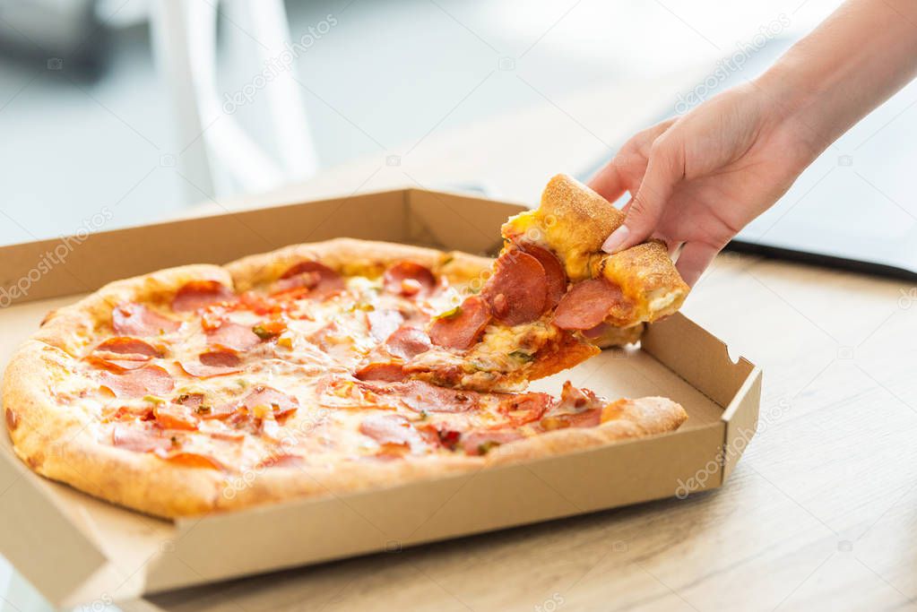 cropped image of woman taking pizza slice from box at table 