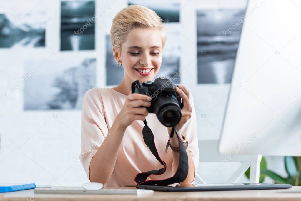 happy female photographer looking at camera screen at table with computer in home office