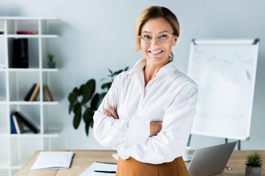 beautiful businesswoman standing with crossed arms in office clipart
