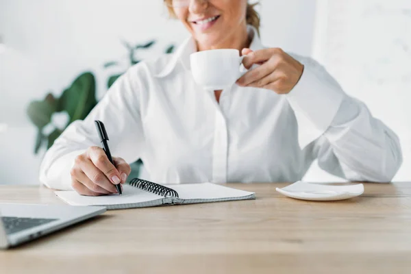 Imagem Cortada Empresária Segurando Xícara Café Escrevendo Para Notebook Escritório — Fotografia de Stock