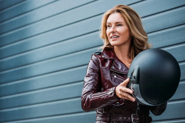 有吸引力的妇女在皮革夹克持有摩托车头盔在街上 看着远离 — 图库照片