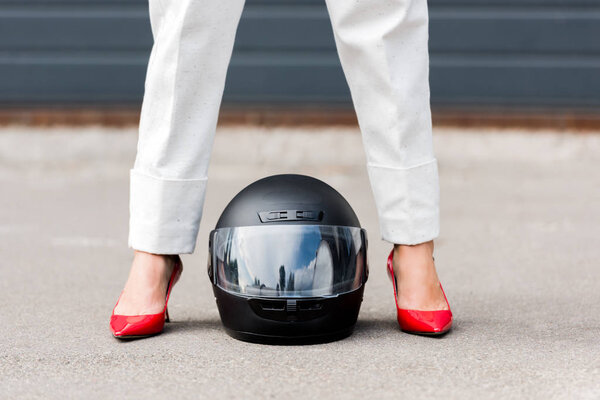 cropped image of woman in red shoes standing near motorcycle helmet on street 