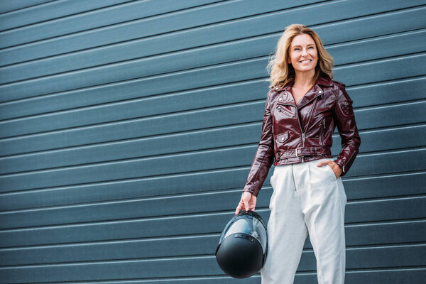 attractive woman in leather jacket holding motorcycle helmet on street 