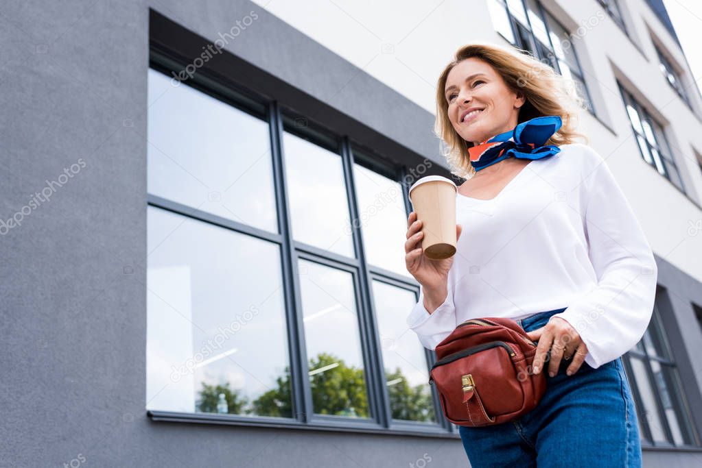 low angle view of attractive woman walking with disposable coffee cup on street 
