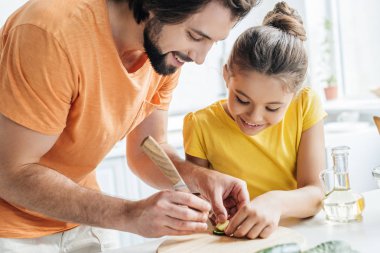 father and daughter carving cucumber while cooking at home together clipart