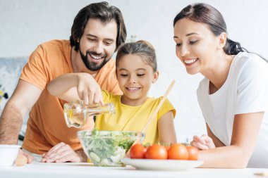 beautiful young family preparing salad together at kitchen clipart