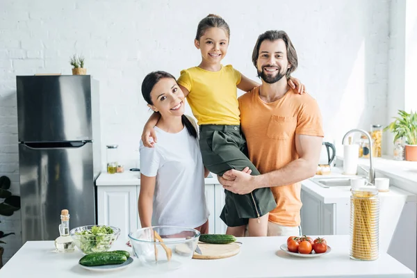 Όμορφη Νεαρή Οικογένεια Αγκαλιάζοντας Στην Κουζίνα Και Βλέπουν Φωτογραφικών Μηχανών — Φωτογραφία Αρχείου