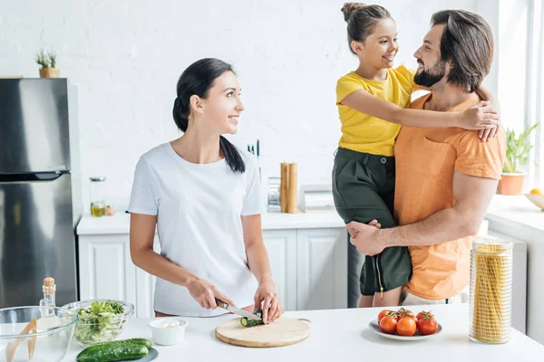 Güzel Genç Kadın Mutfağa Kucaklayan Kızı Eşi Ise Salata Hazırlık — Stok fotoğraf