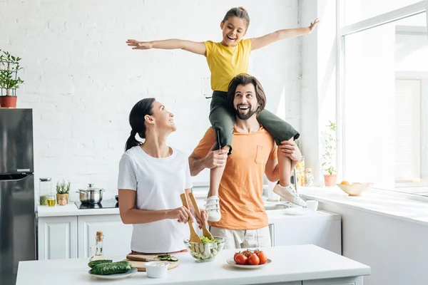 Femeie Tânără Frumoasă Pregătind Salata Timp Fiica Călare Umerii Soțului — Fotografie, imagine de stoc