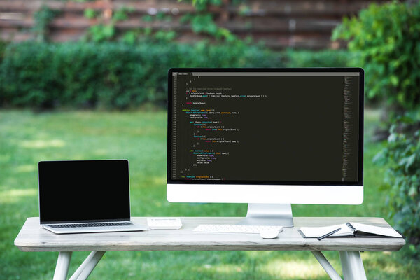 selective focus of laptop with blank screen and computer with programming language code at table outdoors 