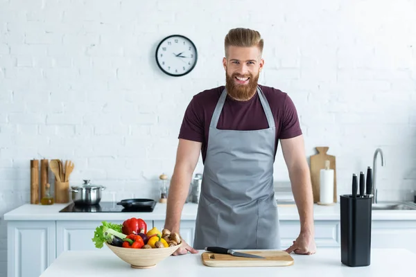 Guapo Barbudo Joven Delantal Sonriendo Cámara Mientras Cocina Cocina —  Fotos de Stock