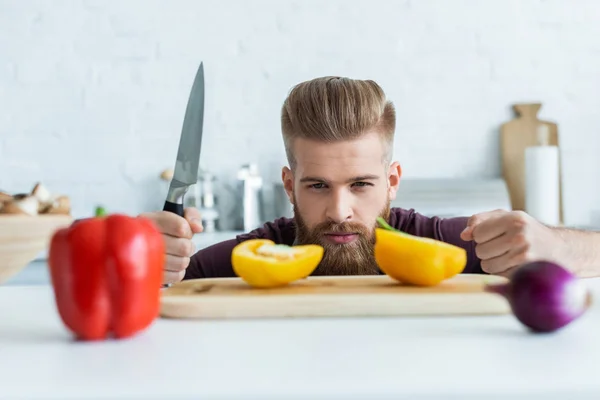 Guapo Barbudo Joven Sosteniendo Cuchillo Mirando Pimientos — Foto de Stock