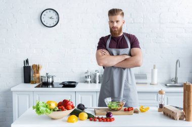 mutfakta yemek yaparken önlük ayakta çapraz kollu yakışıklı sakallı adam