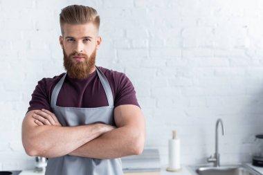 sakallı yakışıklı genç ile çapraz kol ayakta ve mutfak kamerada bakarak önlük