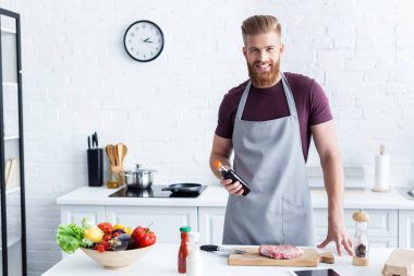 yakışıklı sakallı adam biftek yemek ve mutfak kameraya gülümseyen önlük 