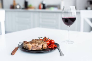delicious steak with cherry tomatoes on plate and glass of red wine on table clipart