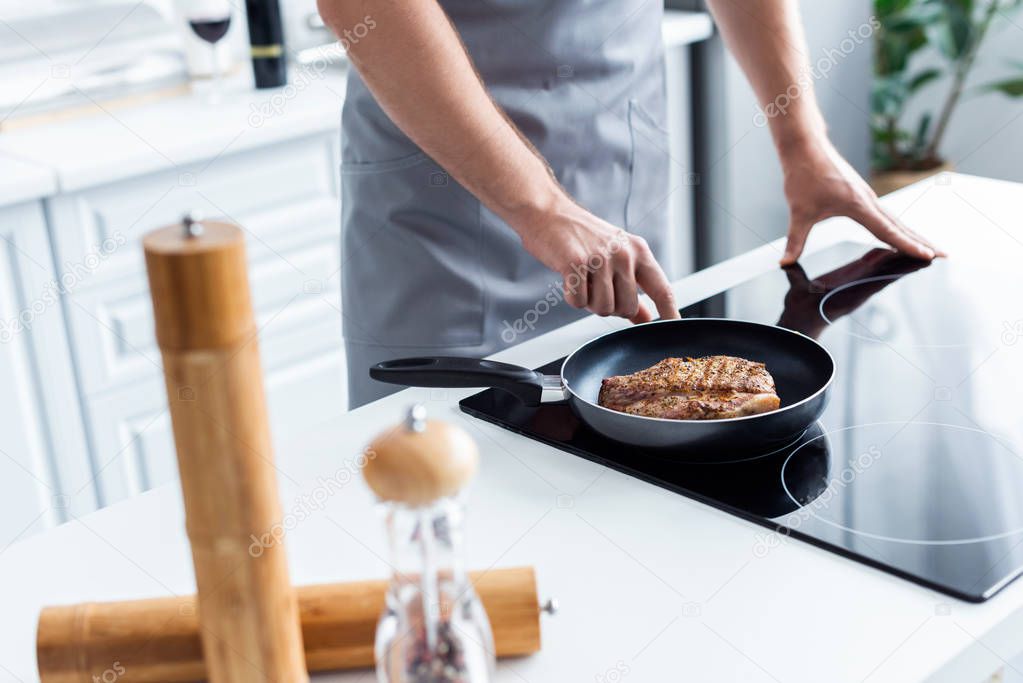 cropped shot of man cooking delicious steak in frying pan on stove