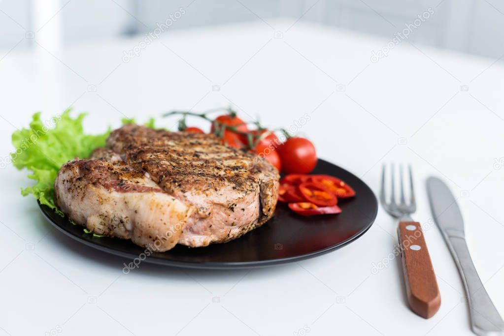 close-up view of delicious grilled steak with lettuce, pepper and cherry tomatoes on black plate