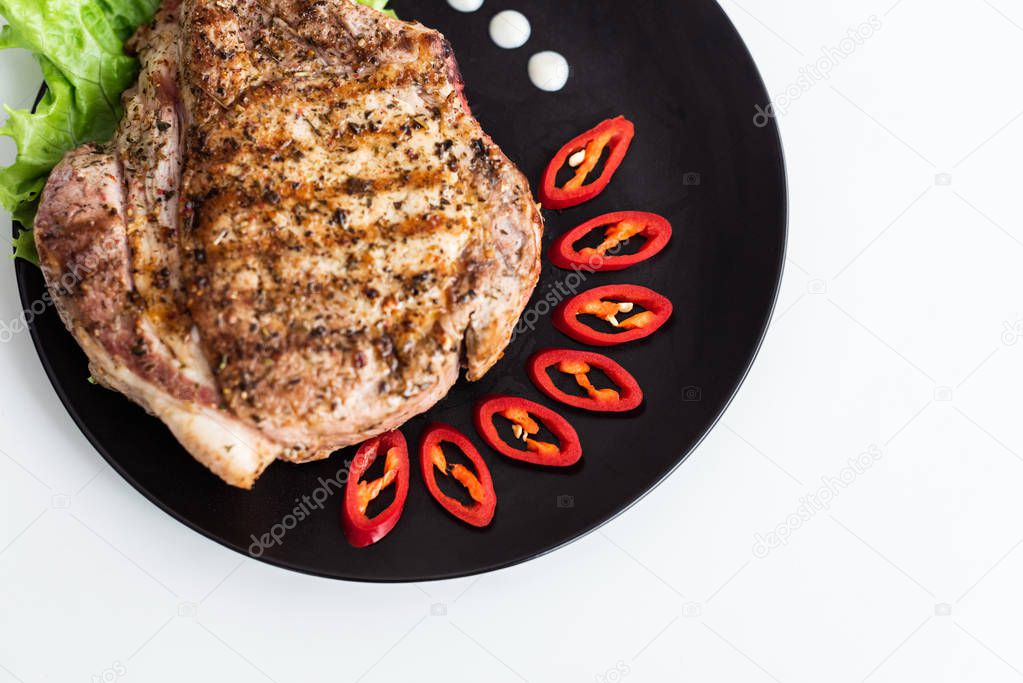 top view of delicious beef steak with sliced pepper, lettuce and sauce on black plate on white