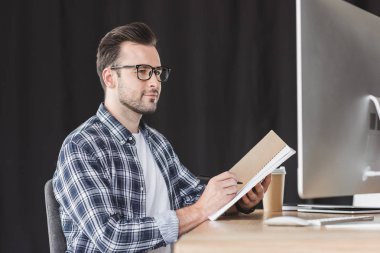 Not defterinde almak ve masaüstü bilgisayar kullanarak gözlük yakışıklı genç programcı
