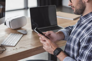 gülümseyen adam işyerinde otururken smartphone kullanarak atış kırpılmış