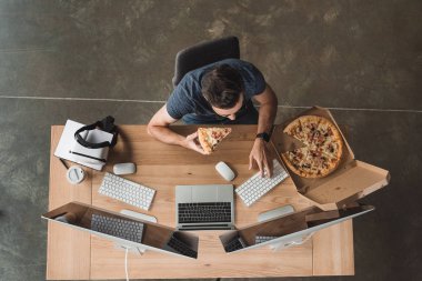overhead view of programmer eating pizza and using computers at workplace clipart