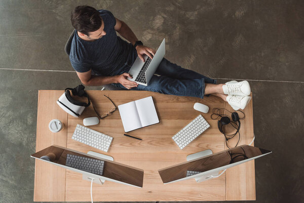 вид сверху на молодого человека с помощью ноутбуков и настольных компьютеров на рабочем месте
 