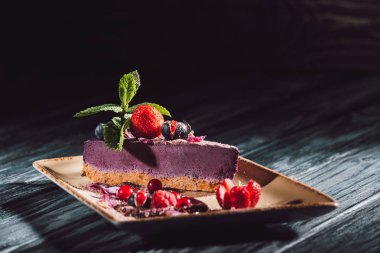 selective focus of blueberry cake with strawberries, mint and viola petals on plate on wooden table 