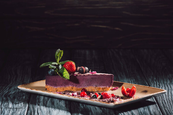 Черничный торт с клубникой, мятой и альтом на тарелке на деревянном столе
 