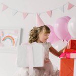 Cute birthday child in cone looking at gift boxes