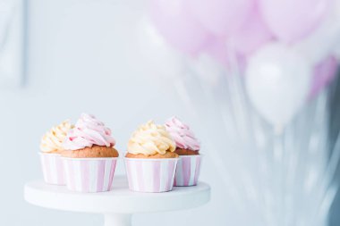 selective focus of stand with delicious cupcakes in front of bunch of air balloons clipart