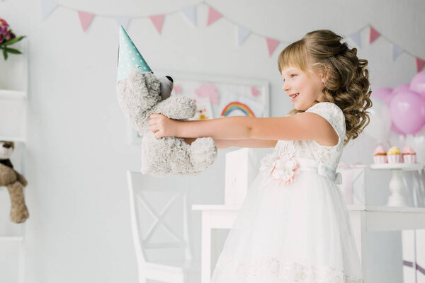 вид сбоку улыбающегося именинника с плюшевым медведем в конусе
