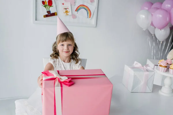 Uśmiechnięte Dziecko Urodziny Kształcie Stożka Siedzi Przy Stole Ogromnym Pudełko — Zdjęcie stockowe