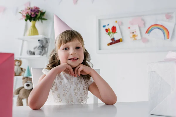 Smiling Birthday Child Cone Looking Camera Sitting Table Gifts — Free Stock Photo