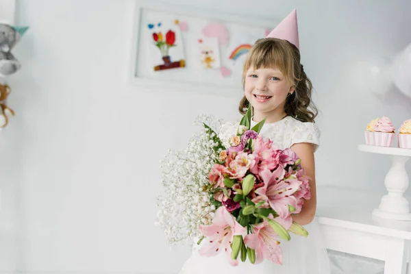 微笑的生日孩子在锥体捧着百合花 — 免费的图库照片