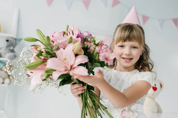 ユリの花束を示す円錐形の愛らしい誕生日子供 — ストック写真