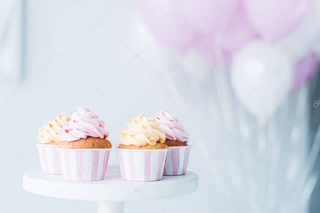 selective focus of stand with delicious cupcakes in front of bunch of air balloons