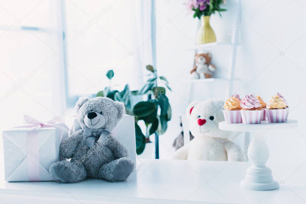 teddy bears on table with present box and cupcakes on stand