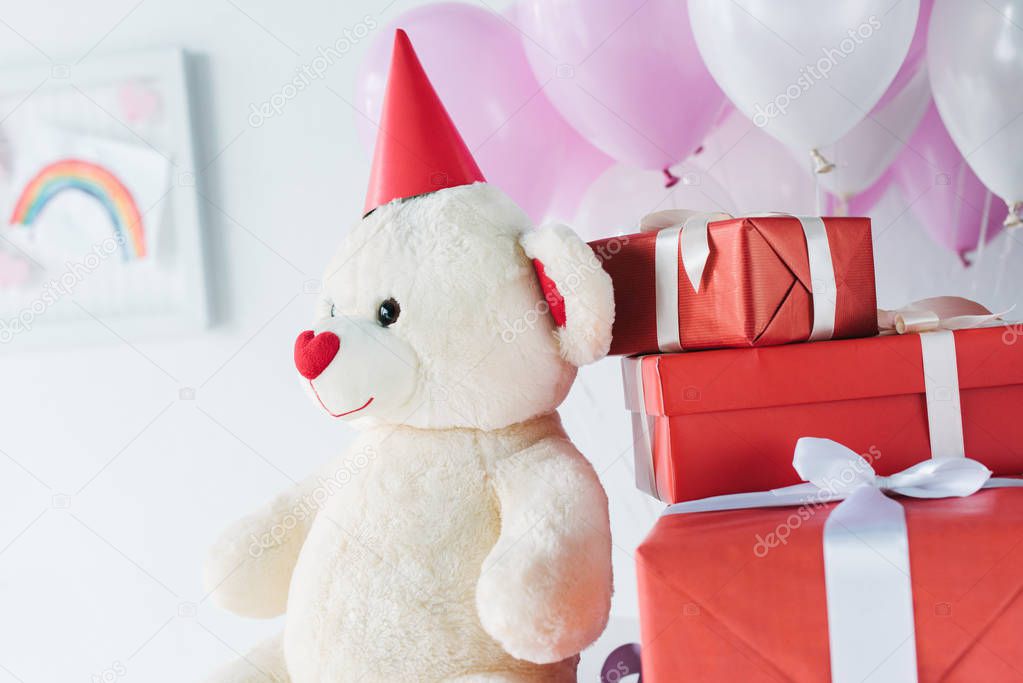 selective focus of teddy bear in cone with gift boxes and air balloons 