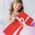 Entzückend lächelndes Kind mit Geschenkschachtel, die von Schleife umwickelt ist