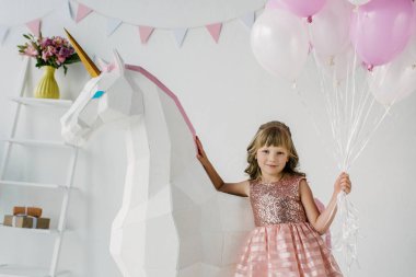 Hava balonları demet tutarak ve dekoratif unicorn ile ayakta çok güzel küçük çocuk 