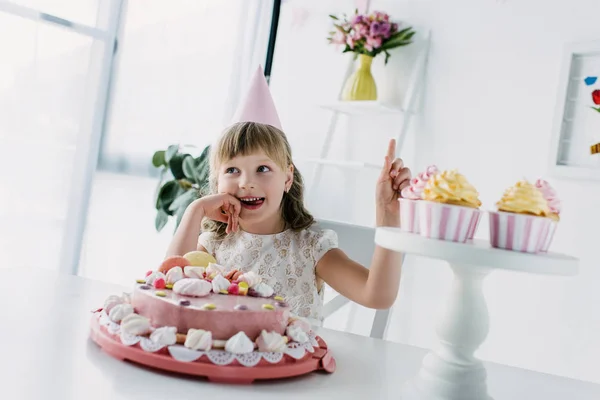 Niño Cumpleaños Sonriente Cono Haciendo Gesto Idea Mientras Está Sentado — Foto de Stock