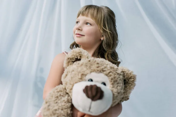 Smiling Little Kid Looking Away Embracing Teddy Bear — Free Stock Photo