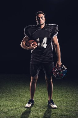 kask ve topu tutarak ve kameraya siyah üzerinde seyir siyah üniformalı emin Amerikan futbolu oyuncusu