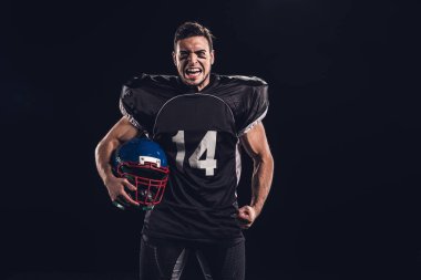 kask tutarak ve siyahta izole kamera seyir siyah üniformalı kızgın Amerikan futbolu oyuncusu