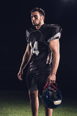 kask tutarak ve uzak seyir siyah siyah üniformalı atletik Amerikan futbolu oyuncusu