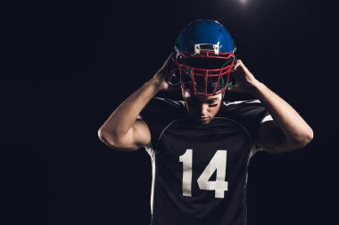 young american football player putting on helmet isolated on black clipart