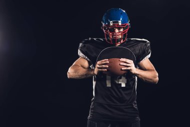 topu elinde tutan ve siyahta izole kamera bakarak emin Amerikan futbolu oyuncusu