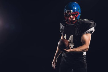 handsome american football player with ball looking at camera isolated on black clipart