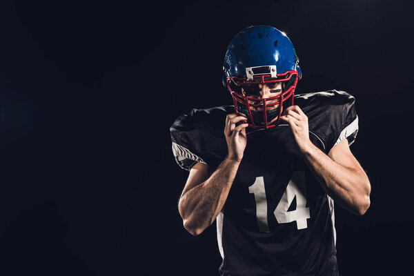 Американский футболист надевает шлем и смотрит на камеру, изолированную на черном
